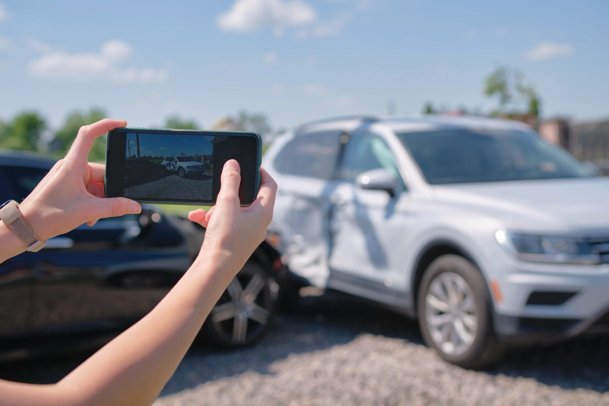 Hands holding a smartphone to photograph a damaged SUV after a car accident, emphasizing the importance of documenting accident scenes.