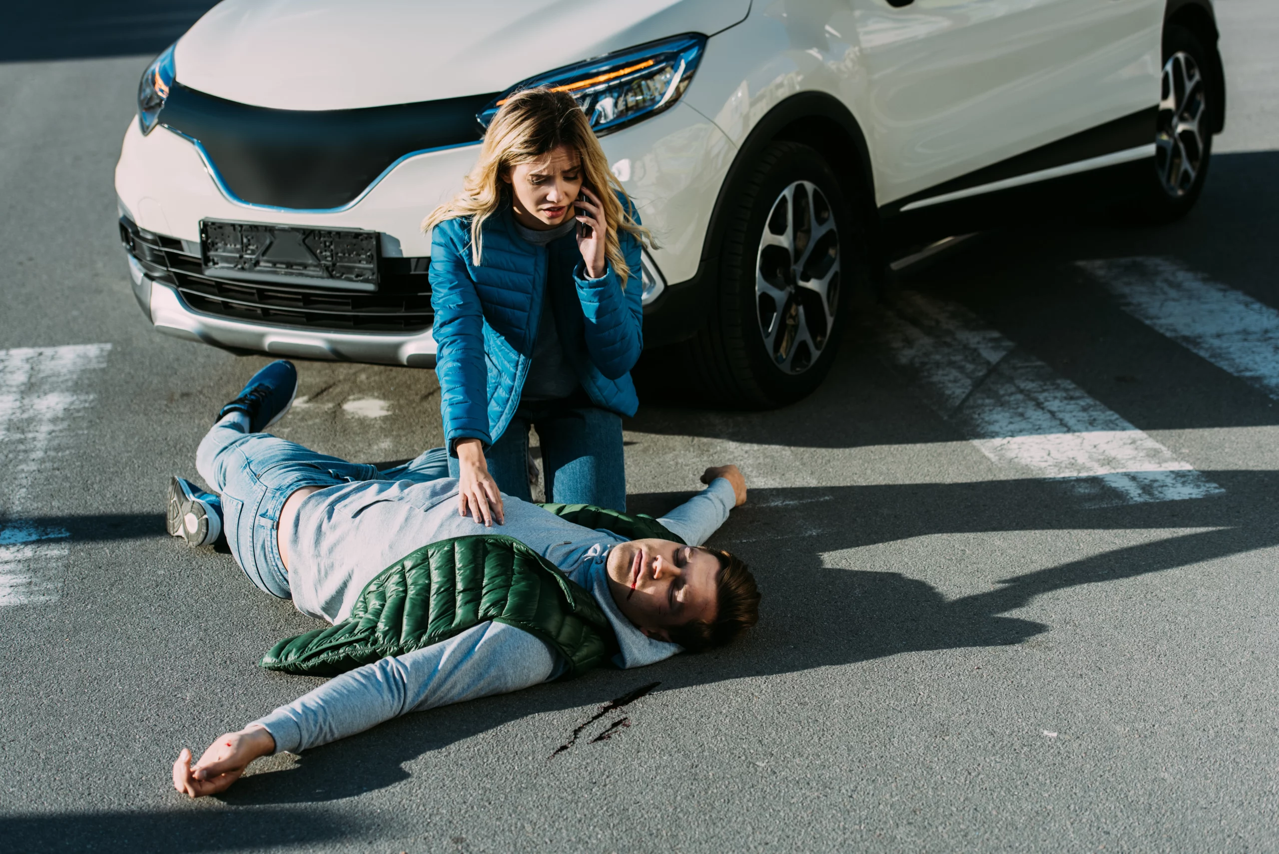 Woman calls for help beside unconscious man at crosswalk after car accident involving uninsured driver in Birmingham.