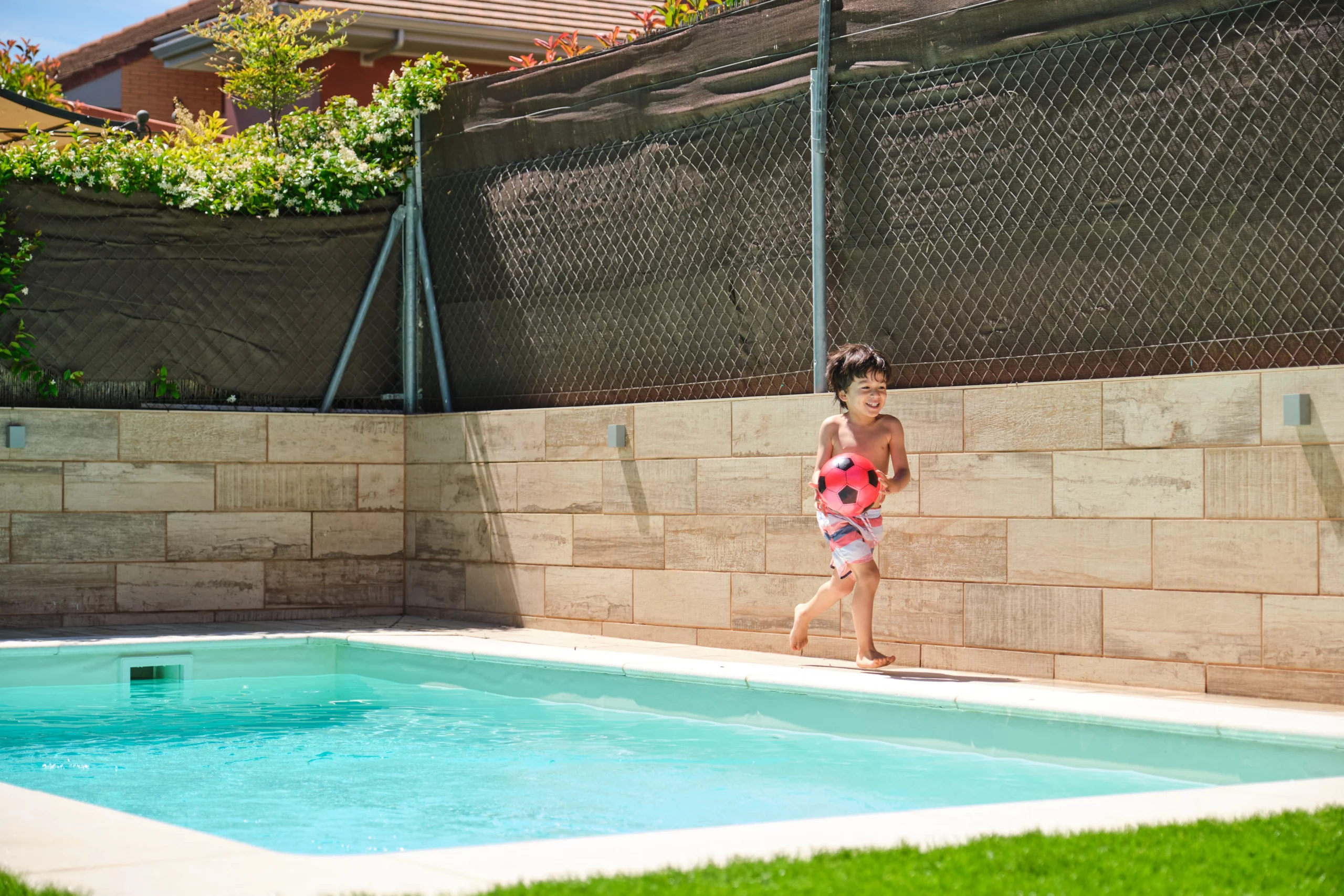 Child running by backyard pool with soccer ball, illustrating attractive nuisance and child safety laws in Alabama