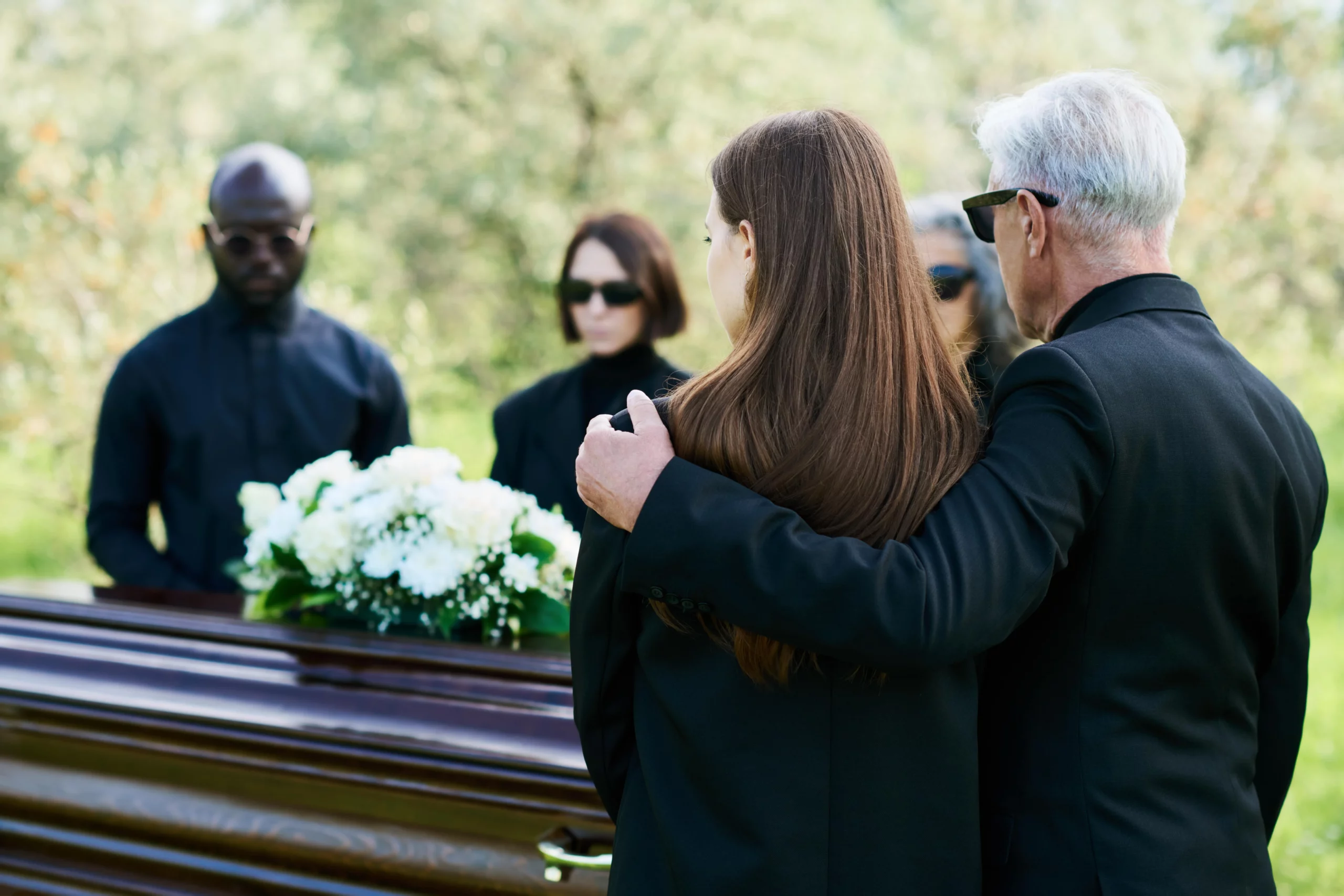Somber funeral scene with people in black gathered around a wooden casket adorned with white flowers — reflecting the emotional and legal gravity of wrongful death claims in Alabama.