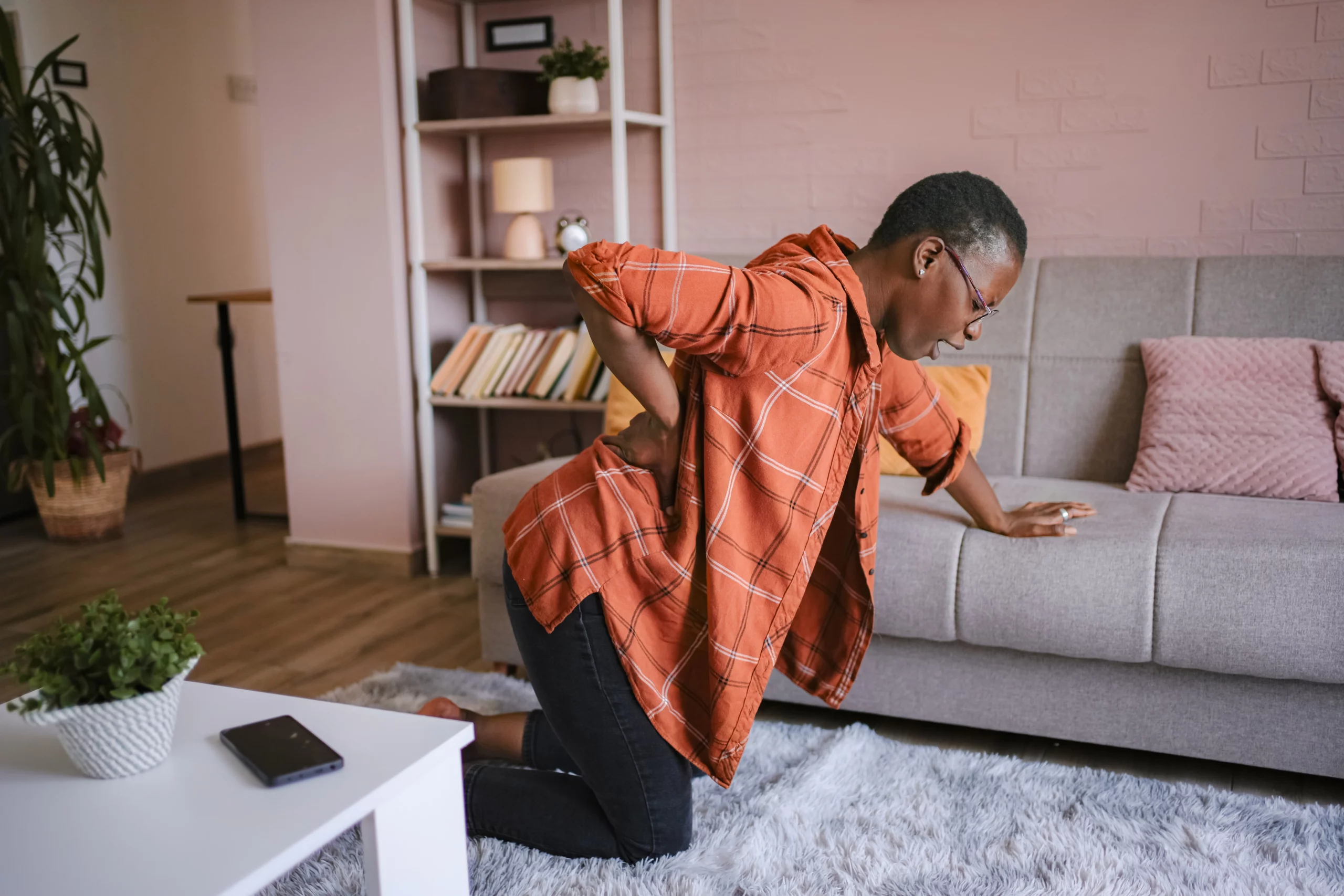Person in orange plaid shirt kneeling on carpet holding lower back in pain, illustrating back injury after a grocery store fall.